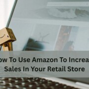 A small cardboard Amazon figure stands on a laptop keyboard in front of an open webpage, with text about using Amazon to increase retail store sales.