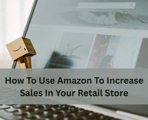 A small cardboard Amazon figure stands on a laptop keyboard in front of an open webpage, with text about using Amazon to increase retail store sales.