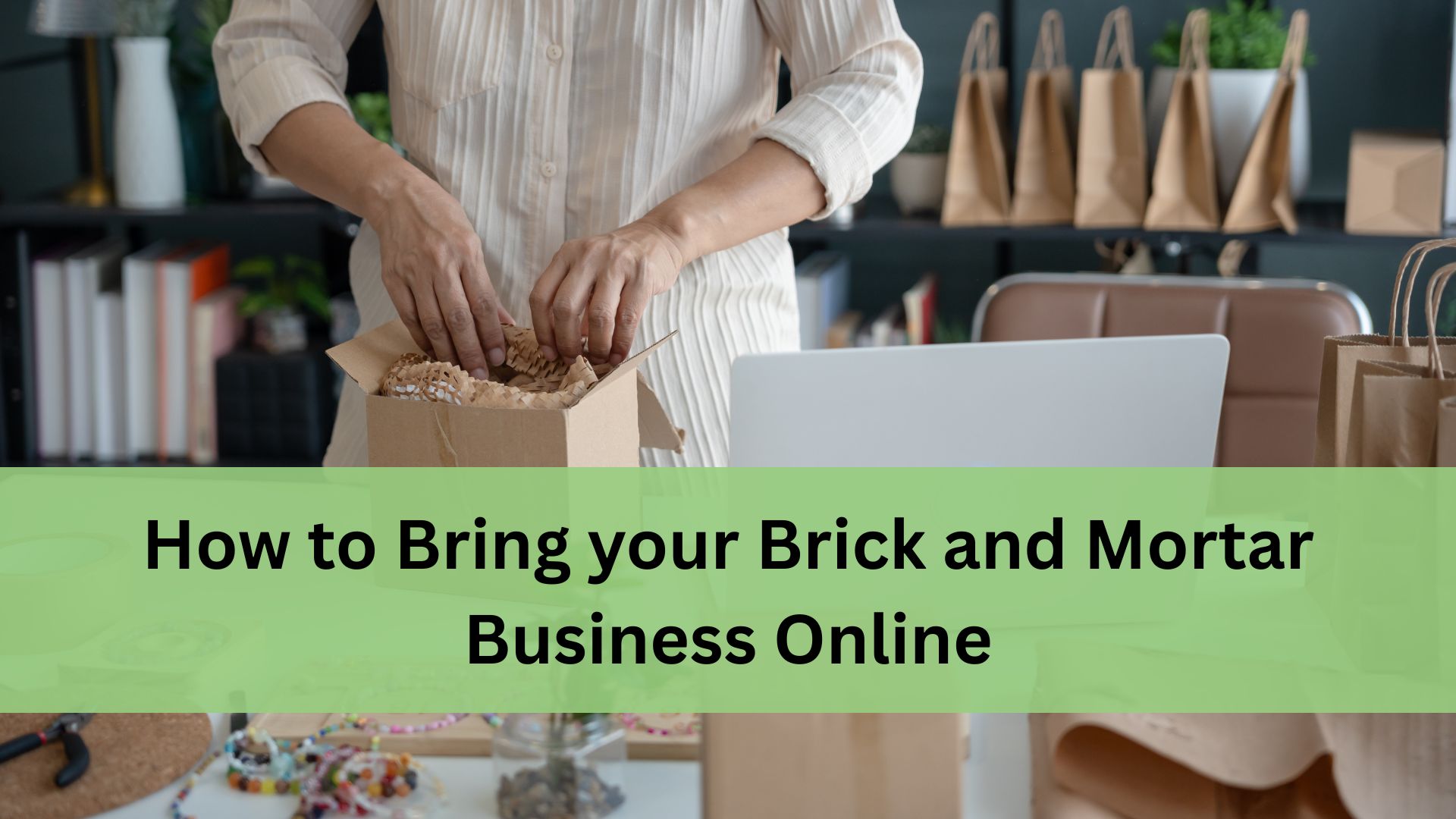A small business owner packs products into a cardboard box at a desk with a laptop and shopping bags in the background.