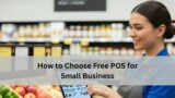 A grocery store employee in a blue uniform smiles while using a free POS system in front of produce and shelves