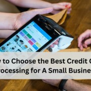 Close up of hands using a handheld point of sale terminal on a wooden counter, with a text banner that reads “How to Choose the Best Credit Card Processing for A Small Business.”