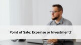 Blurred view of a man working at a desk with a laptop, representing the question of whether a POS system is an expense or an investment