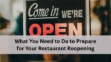 A close up of a storefront sign that says "Come in We're Open" with a blurred restaurant interior in the background.