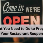 A close up of a storefront sign that says "Come in We're Open" with a blurred restaurant interior in the background.