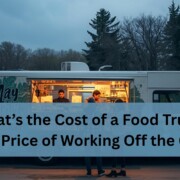 A food truck parked outdoors at dusk with warm light glowing from the service window. Two workers inside prepare food while customers stand outside placing orders.