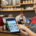 A smiling server in a red shirt and grey apron holds a free point of sale device, taking an order in a coffee shop.