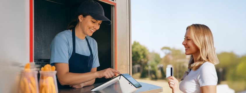 Smiling food truck employee assisting a customer with a credit card payment on a POS payment terminal